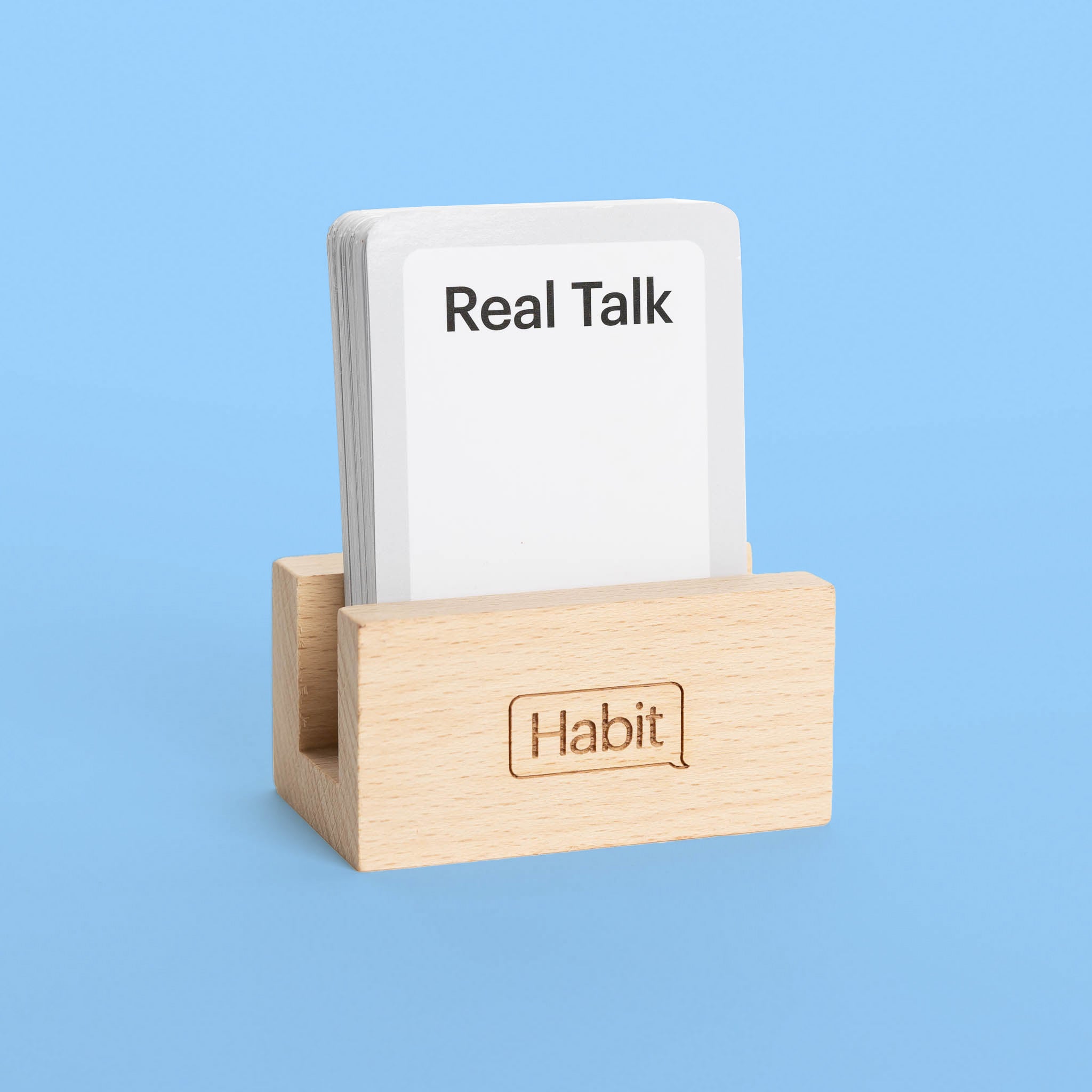 A wooden stand with the text ' Habit ' on it, holding a deck of cards labeled 'Real Talk', conversation card game, building connection with friends, deepening relationship