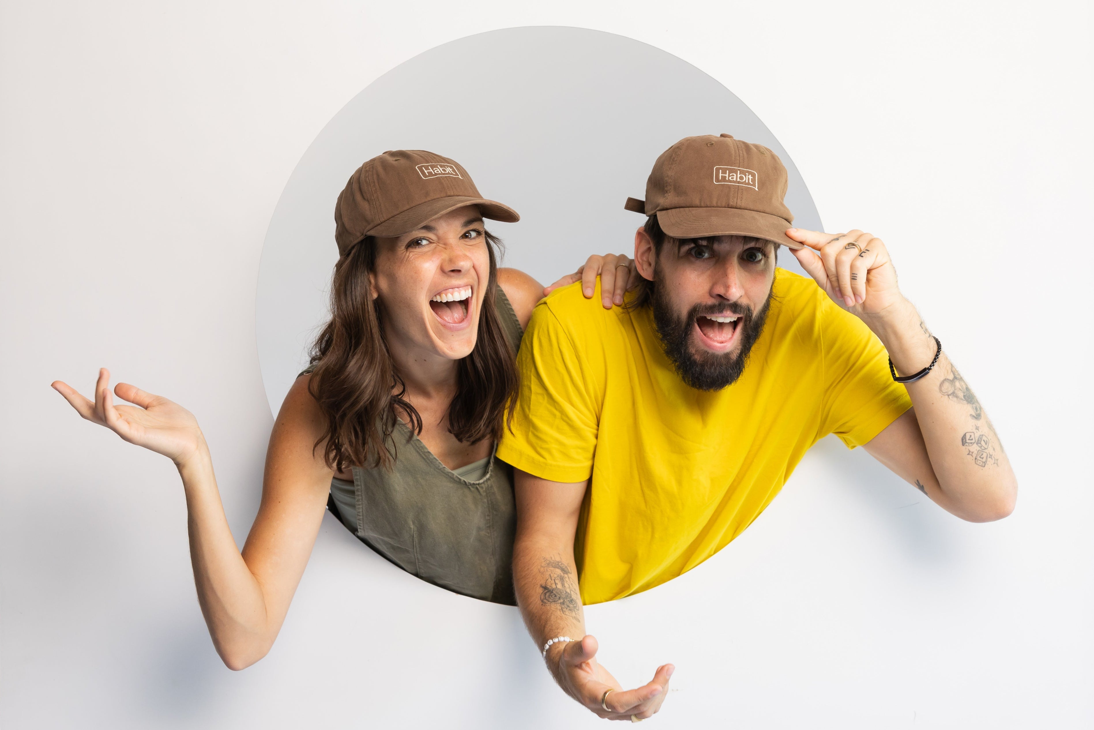 Eamon and Bec, Two people wearing brown baseball caps posing in front of a white backdrop