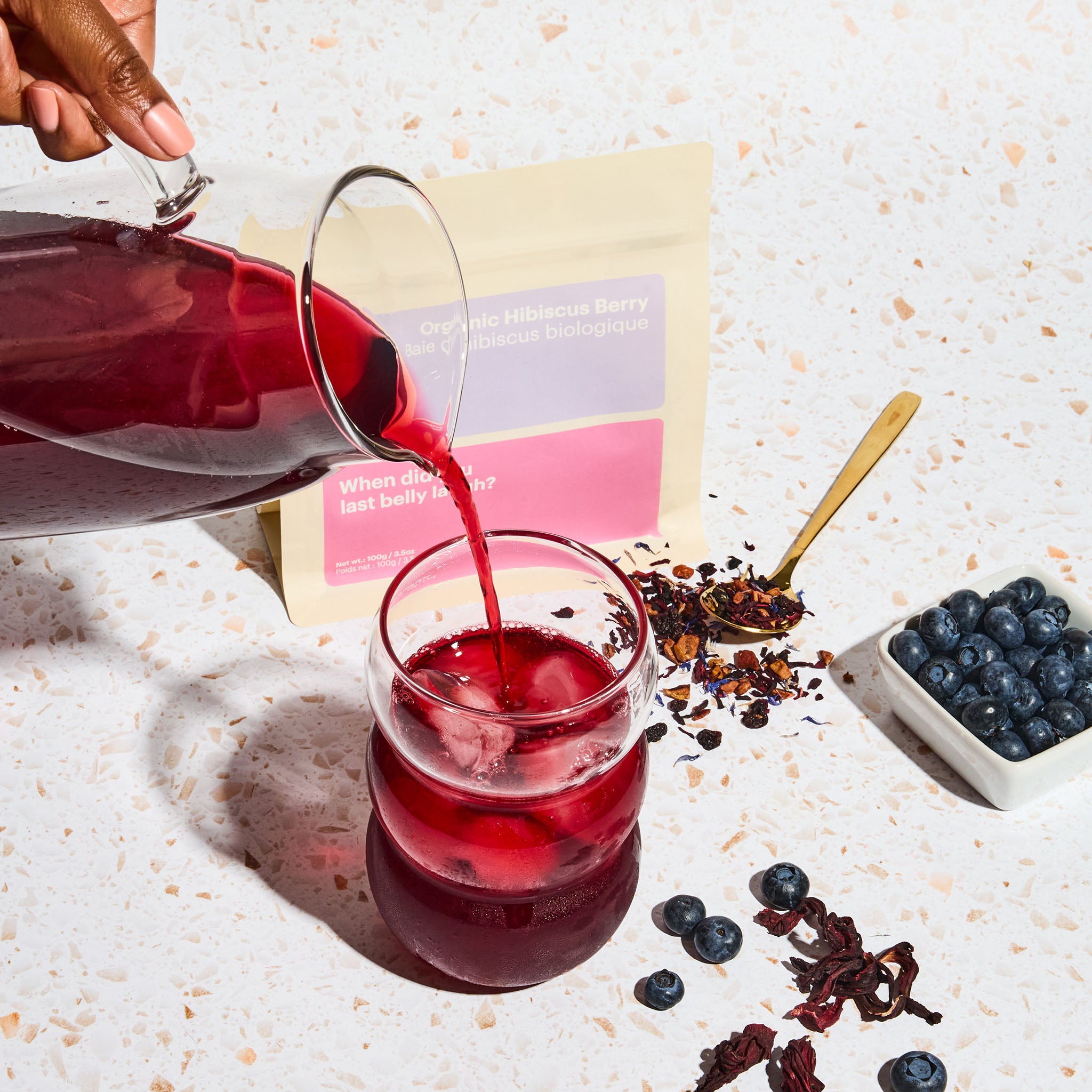 Organic Hibiscus Berry iced tea, iced tea pitcher pouring tea into cup, blueberry, loose leaf tea, gold spoon