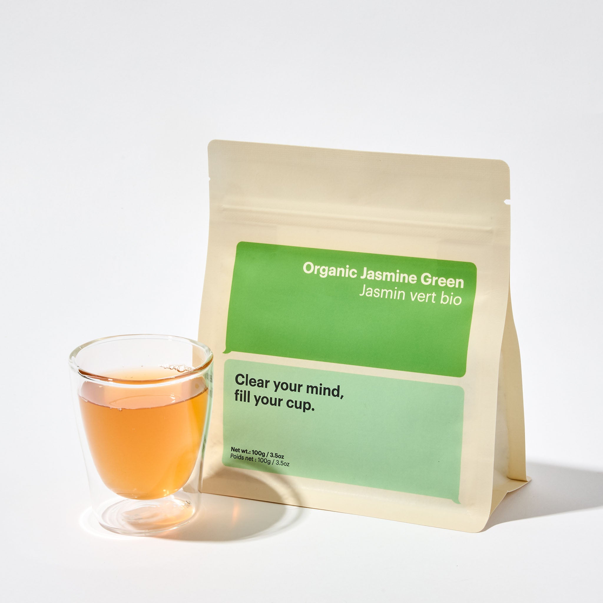 A package of Organic Jasmine Green loose leaf tea with wording on packing to incite deep conversation " clear your mind, fill your cup", cup of Jasmine Green tea next to package