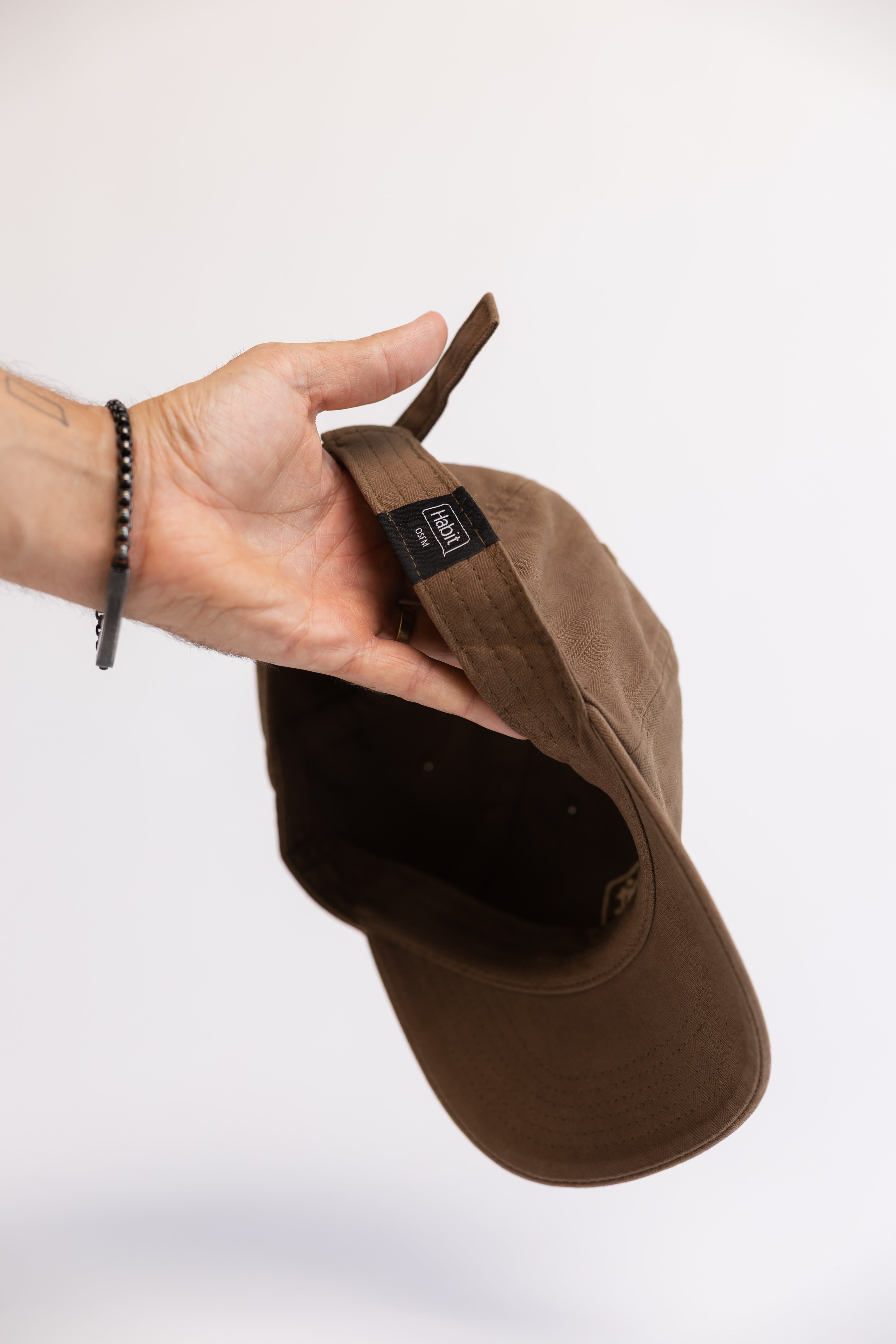 Brown cap held by a hand on a white background, one size fits all baseball cap, merch, stylish and comfortable hat