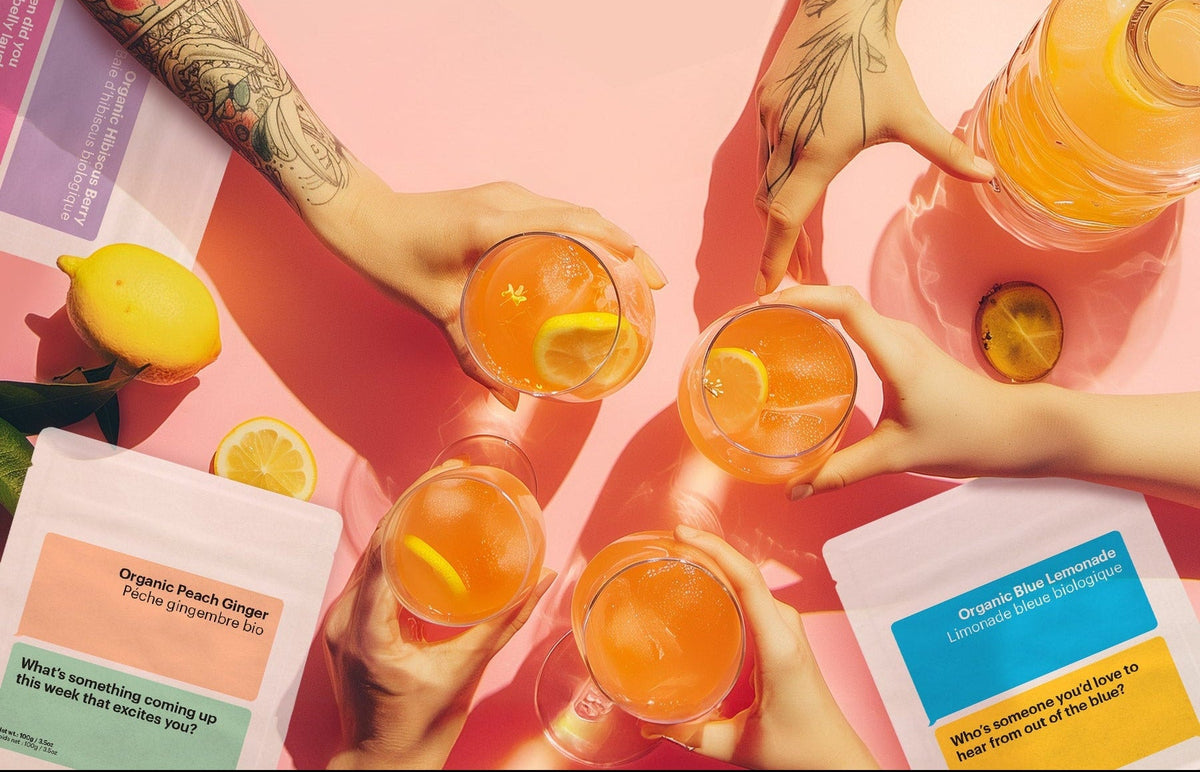 Two hands holding glasses of orange juice with lemons on a pink background